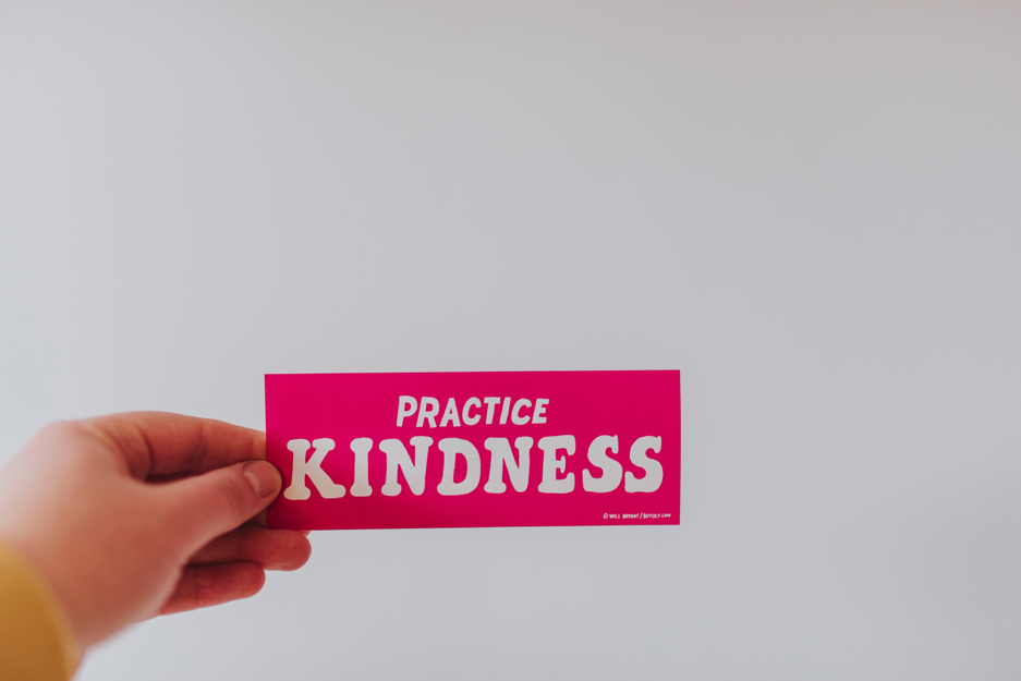 Hand holding up a pink slip that says "Practise Kindness"